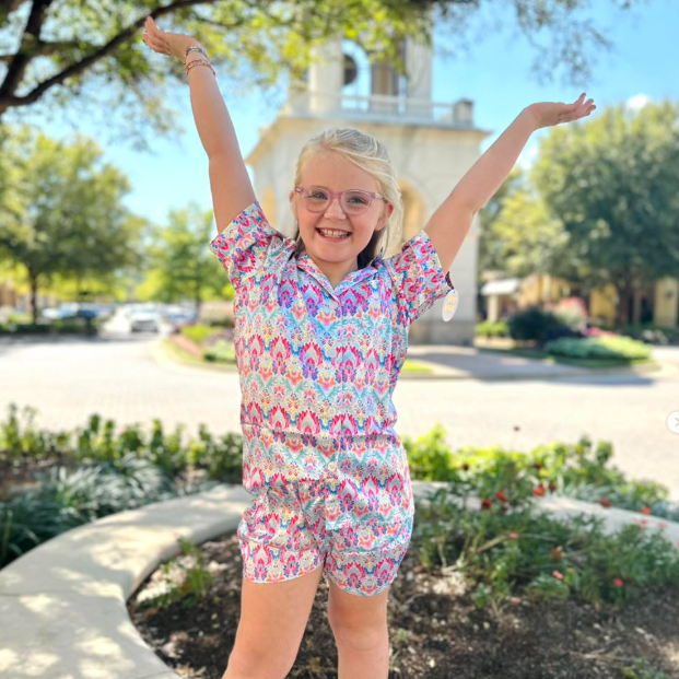 Young girl in a colorful outfit with arms raised outdoors